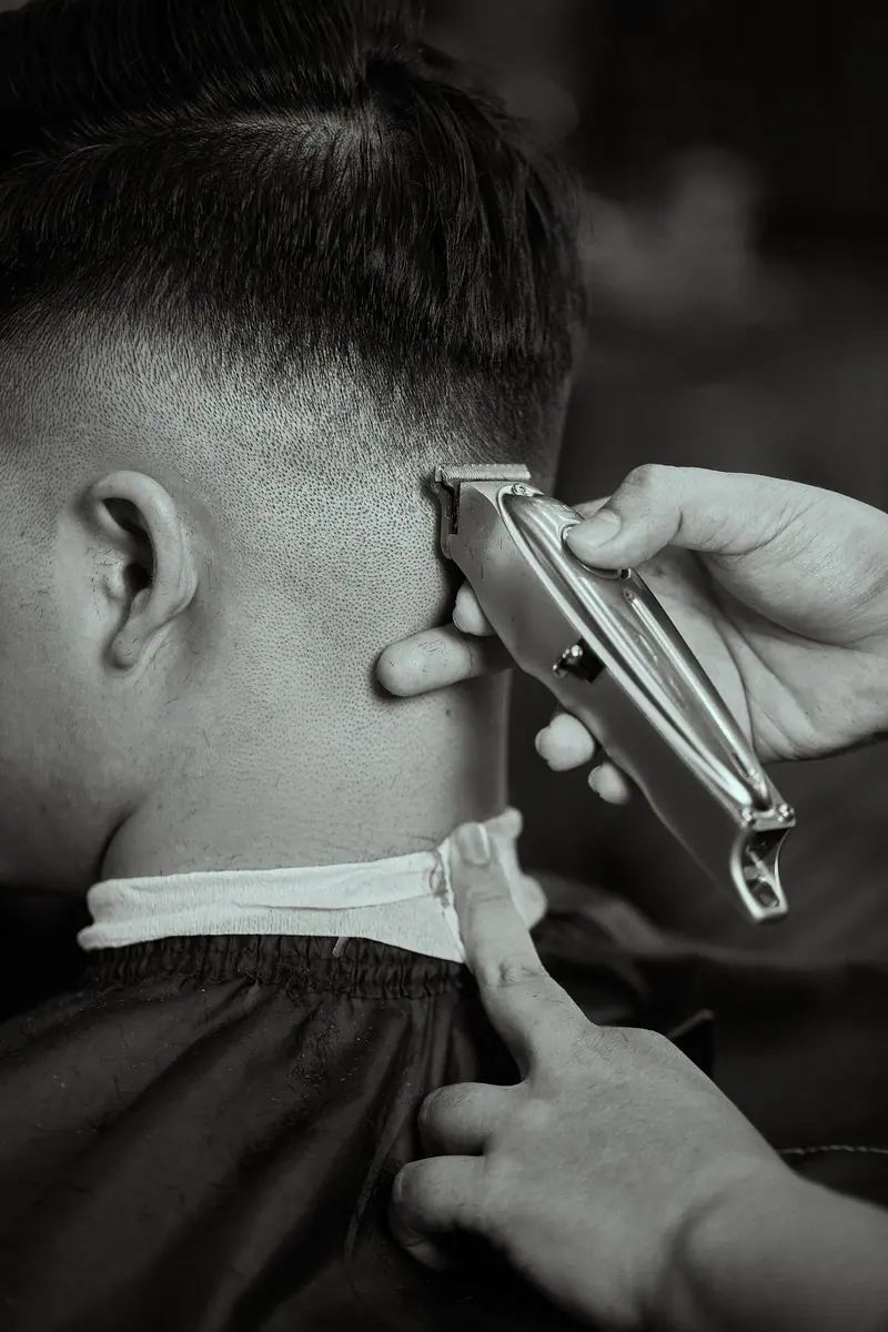 Detailed black and white close-up of a barber trimming a man's hair with clippers.