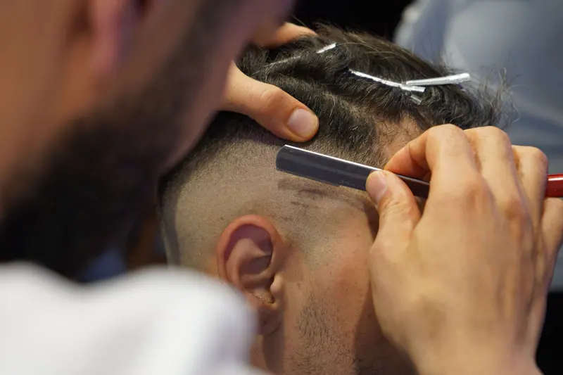 Close-up of a barber giving a modern haircut with a straight razor in a salon.
