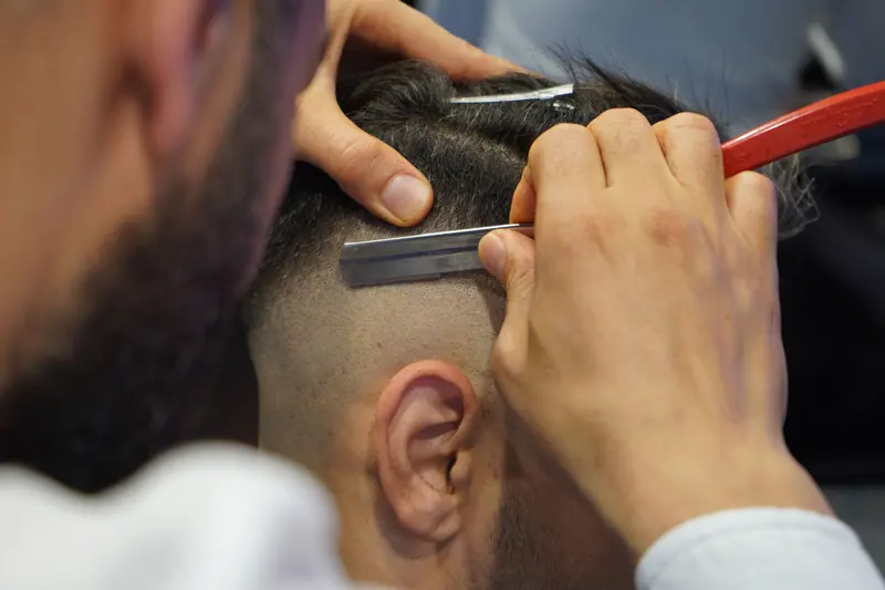 A close-up view of a barber shaving a man's hair with a straight razor.