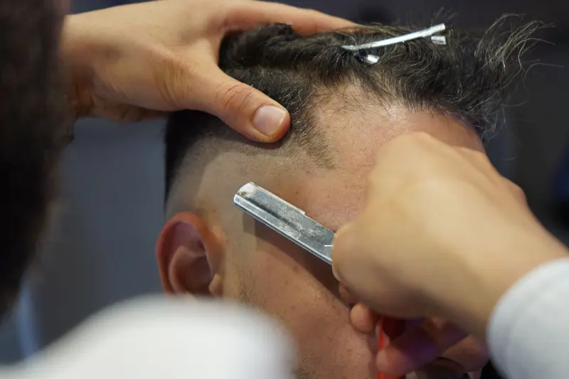 Close-up of a barber expertly using a razor for a precise fade haircut on a customer.