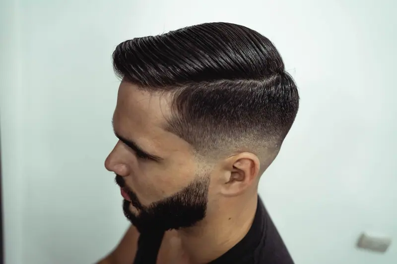 Close-up shot of a man's stylish haircut and beard, showcasing grooming precision.