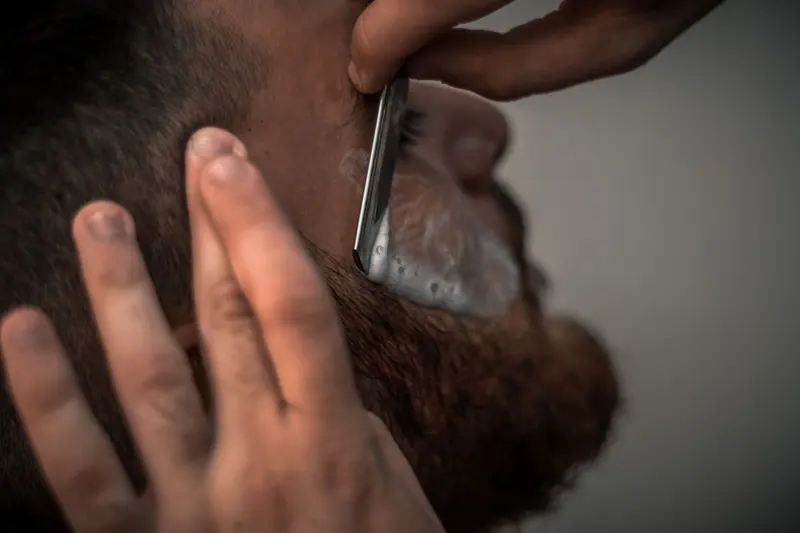 Detailed close-up image of a barber using a razor for precise beard trimming in the barbershop.
