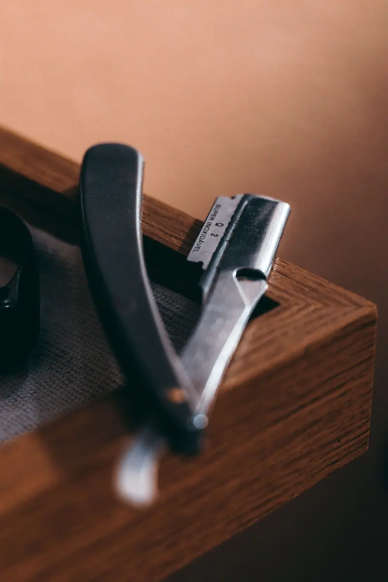Close-up of a classic straight razor resting on a wooden surface, with a warm and moody ambiance.
