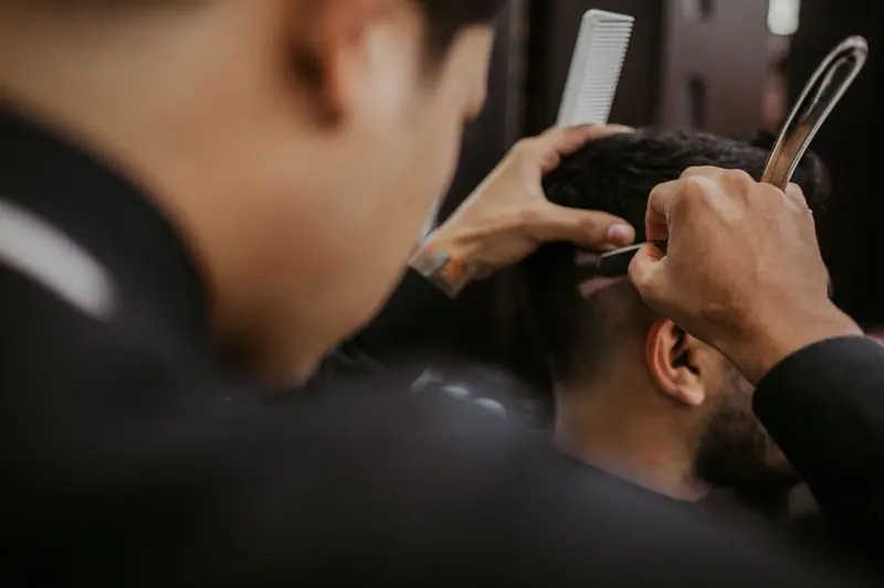 Close-up of a barber expertly styling a man's hair with a razor and comb in a trendy barbershop.