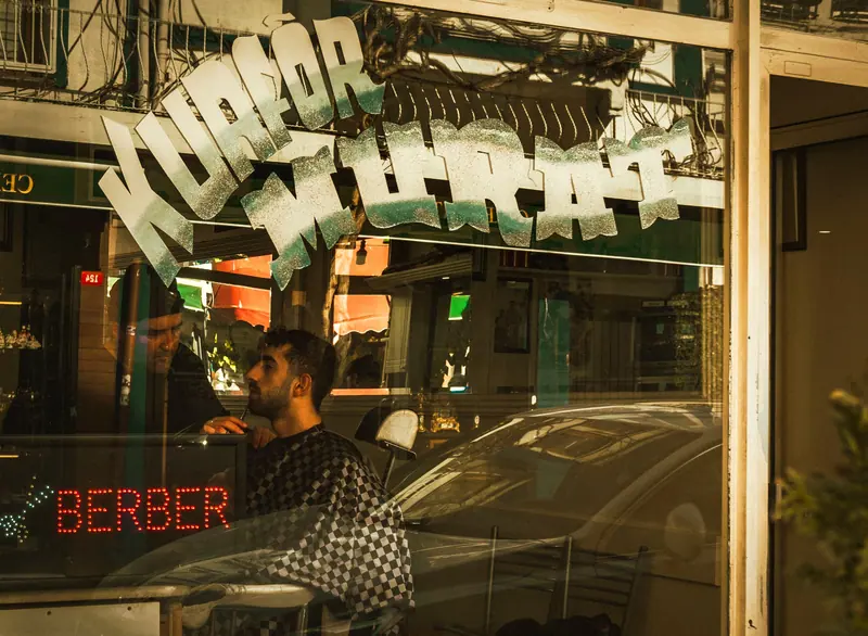 Man getting a haircut in a barbershop with reflective window signage.