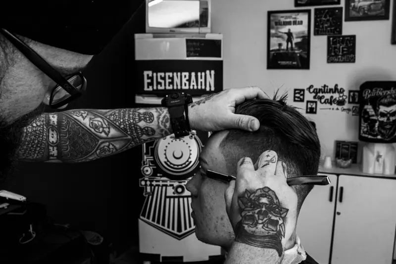 Tattooed barber gives haircut to customer in a stylish barbershop in Colombo, Brazil.
