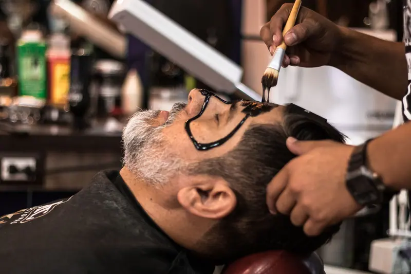 A barber applies a facial mask to a man in a salon, promoting relaxation and skincare.