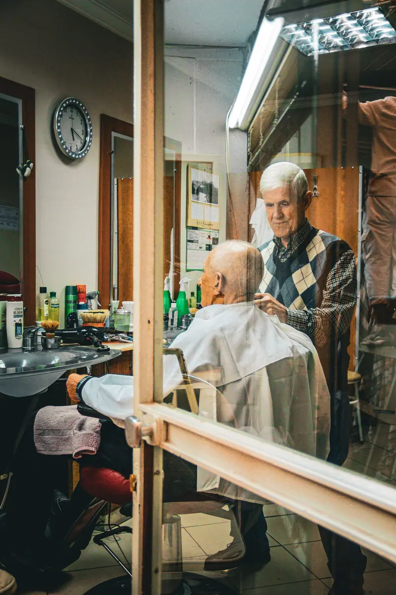 A senior man getting a haircut in a traditional barbershop setting.