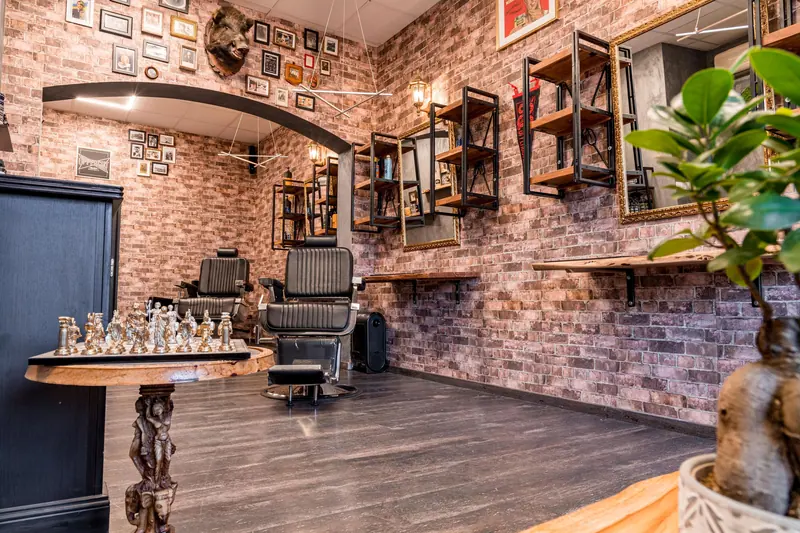 Stylish barbershop room featuring a chess set, leather chairs, shelves, and brick walls.
