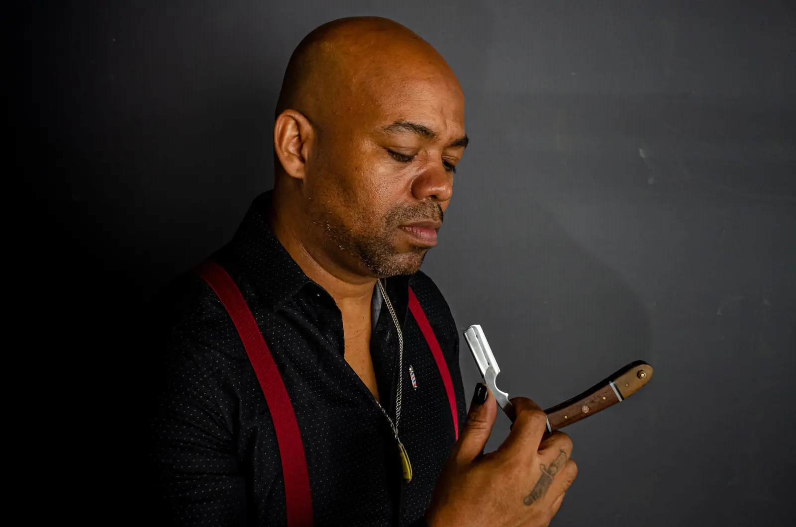 Barber holding a straight razor against a dark backdrop