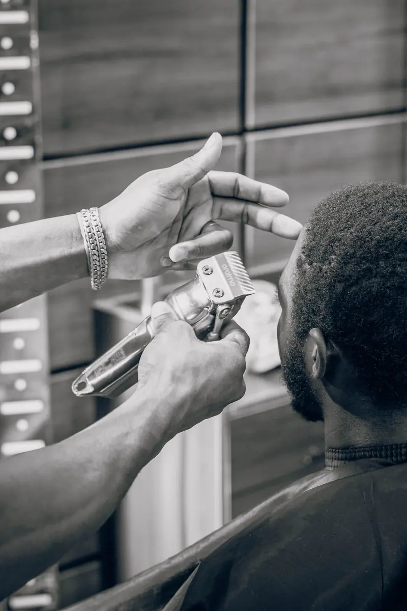Black and white photo of a barber trimming a client's hair with electric clippers in a modern salon setting.