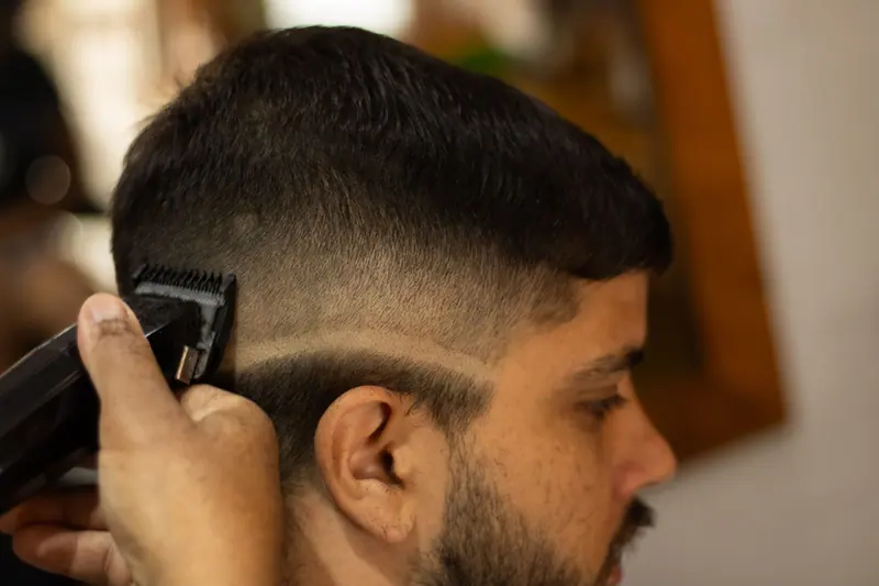 Close-up of a man's head receiving a stylish haircut with trimmers in a barbershop.
