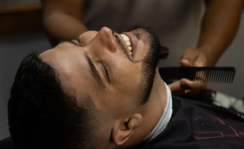 Smiling man receiving a haircut at a barbershop, showcasing a vibrant and relaxed atmosphere.