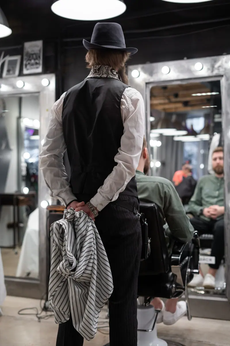 Barber in casual attire with hat and towel preparing for haircut in a trendy barbershop.