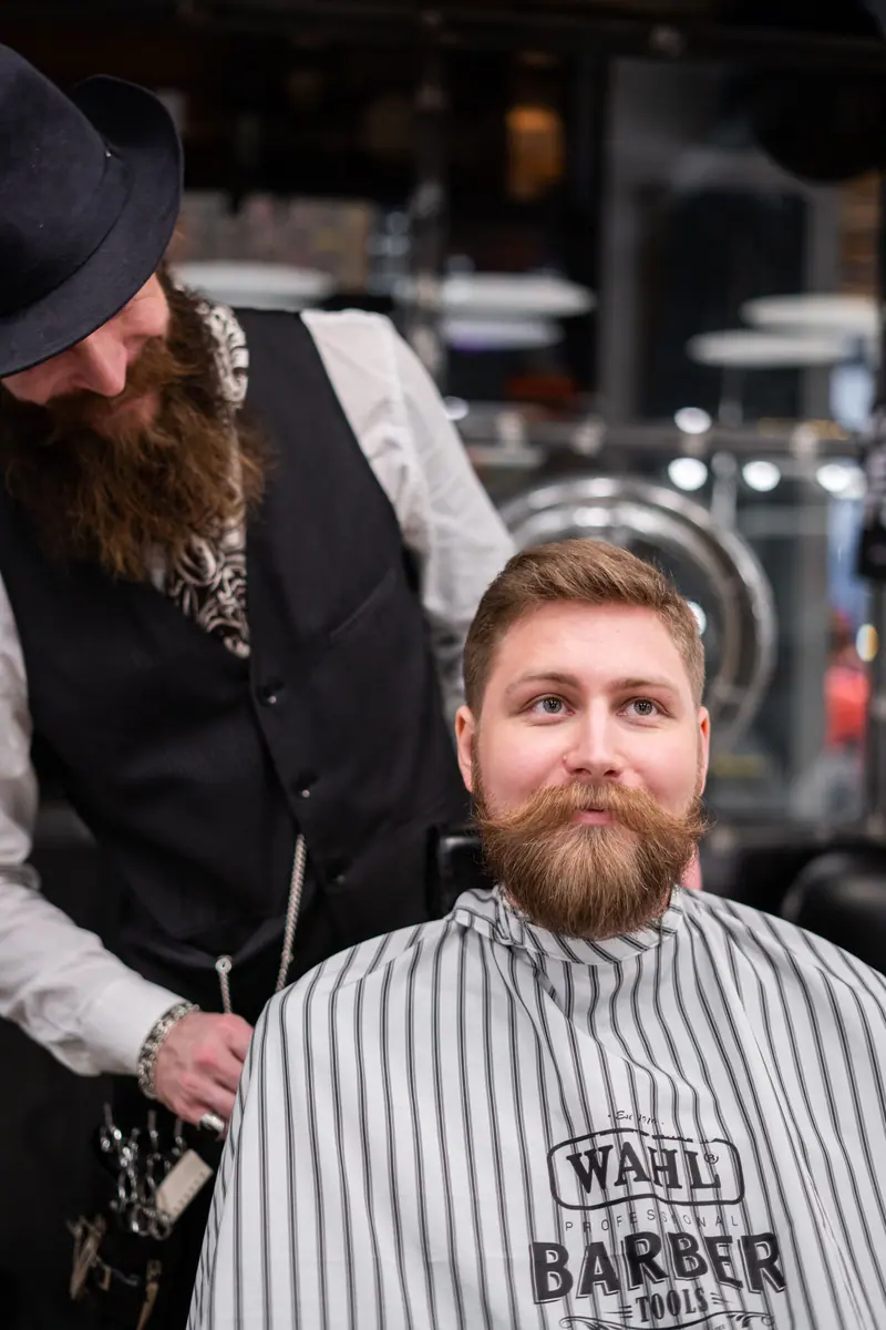 A bearded man receives a stylish beard trim at a modern barbershop.