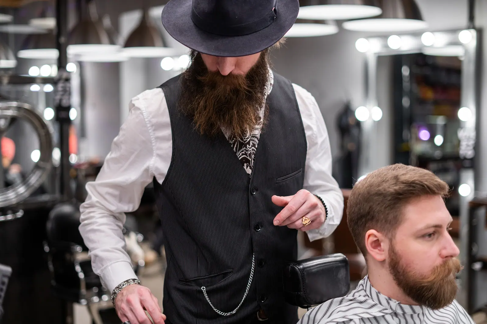 A bearded barber skillfully trims a client's hair in a modern barbershop setting.