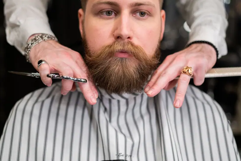 A stylish bearded man receiving precision grooming at a barbershop.
