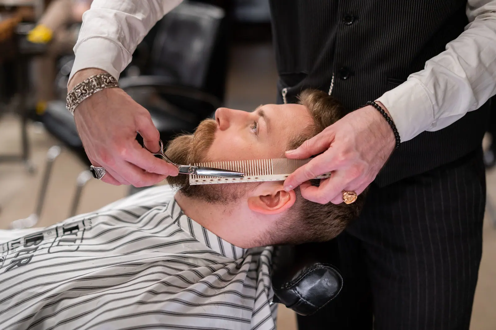 A skilled barber meticulously trims a client's beard using comb and scissors in a modern barbershop.