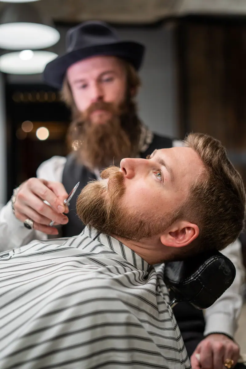 Focused barber prepares to shave a bearded client in a stylish barbershop setting.