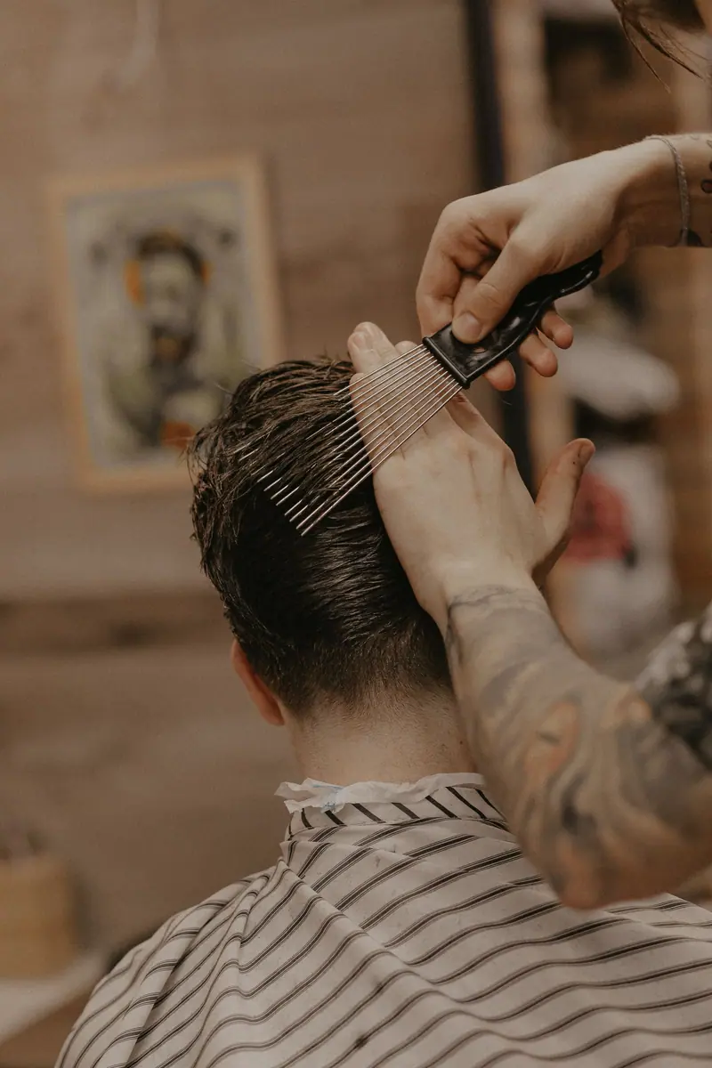 A barber giving a stylish haircut to a man in a rustic barbershop setting, featuring close-up grooming.