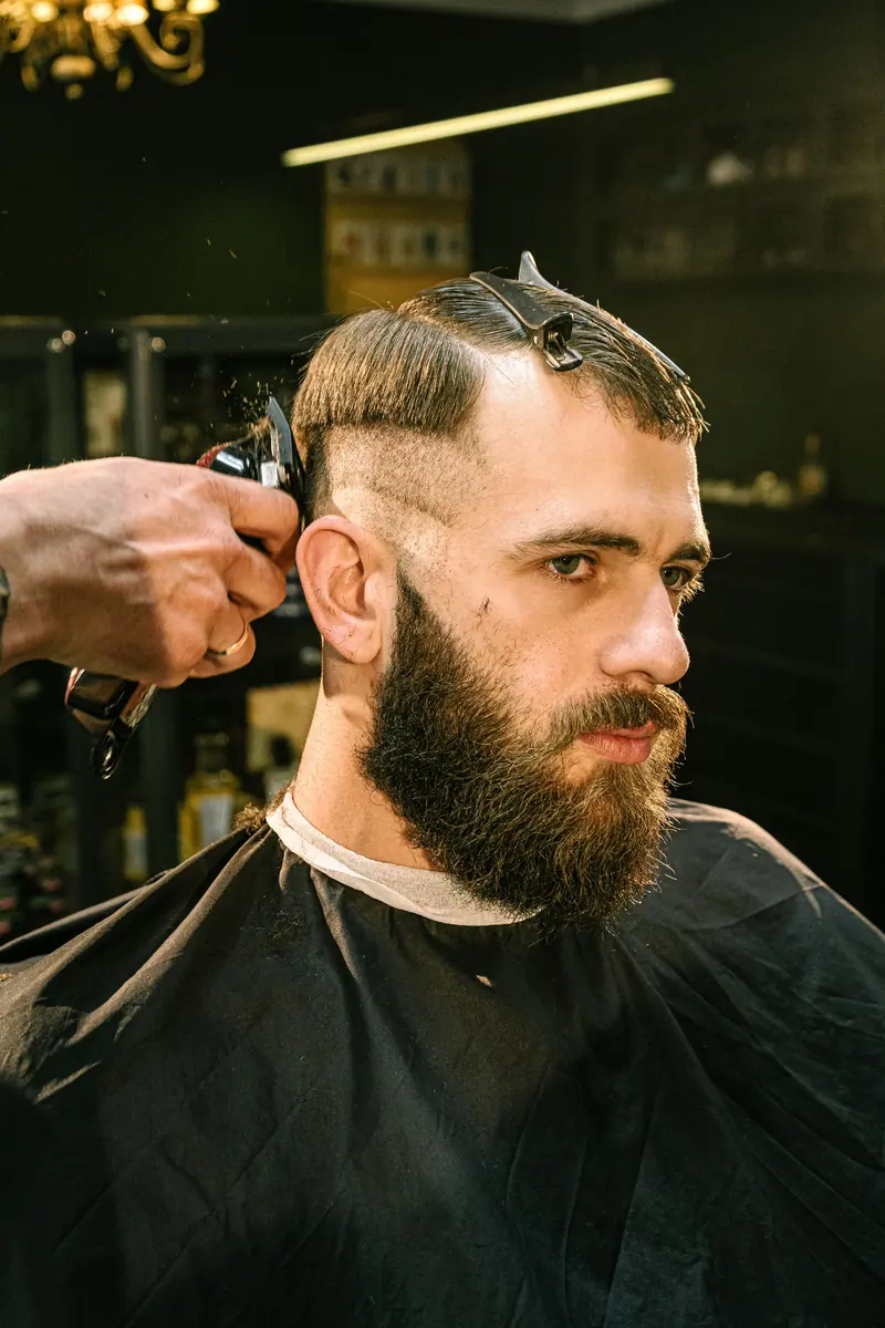 A man receives a haircut and trim in a professional barbershop setting with focus on style and detail.