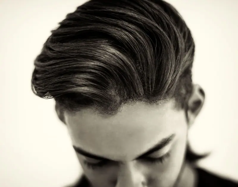 Close-up portrait of a fashionable man showcasing a sleek hairstyle in a black and white studio shot.