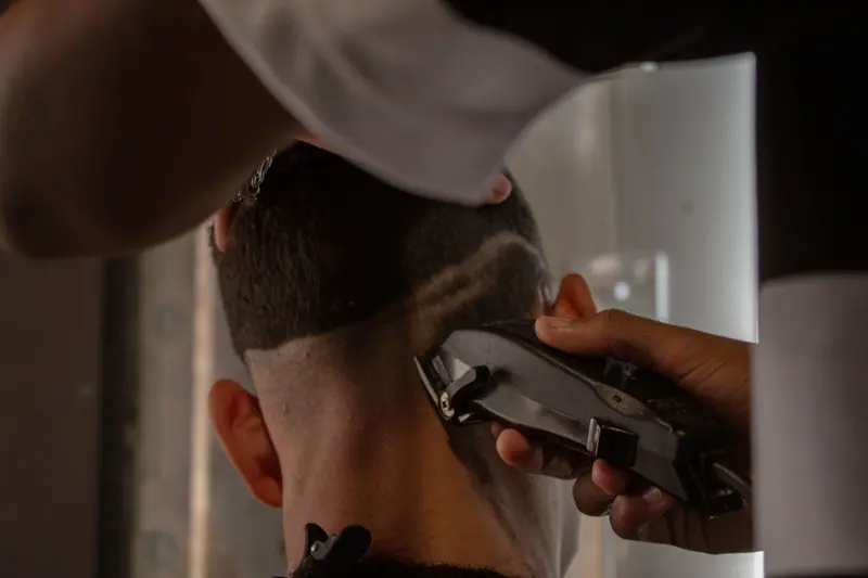A detailed view of a barber using clippers to trim a man's hair indoors.