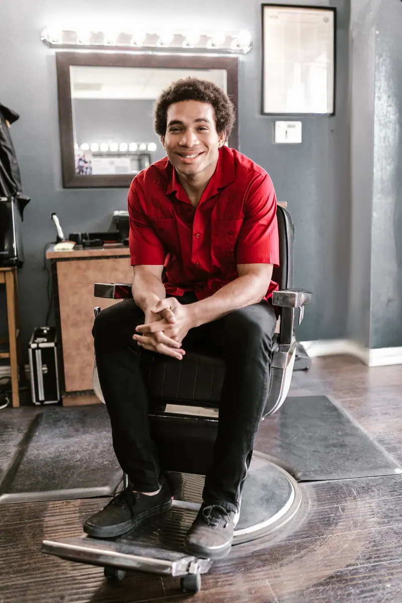 Friendly barber in a bright barbershop environment, sitting and smiling.