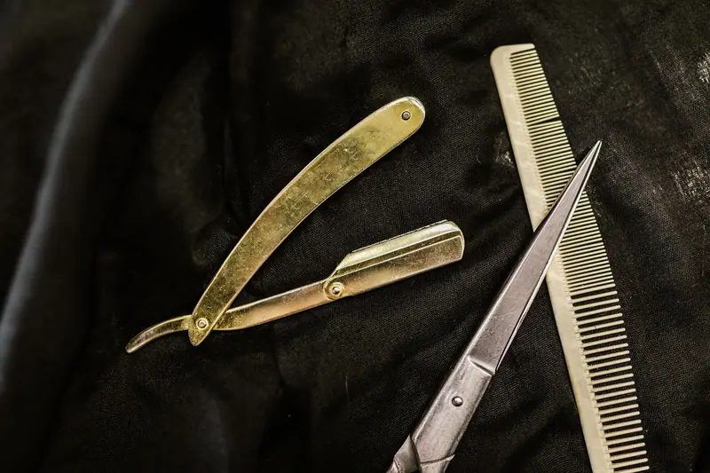 Close-up of silver shears, comb, and straight razor on a black cloth background, highlighting barber tools.
