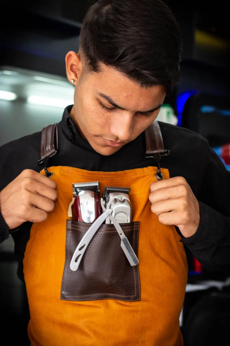 Young barber checking tools in apron. Professional and focused.