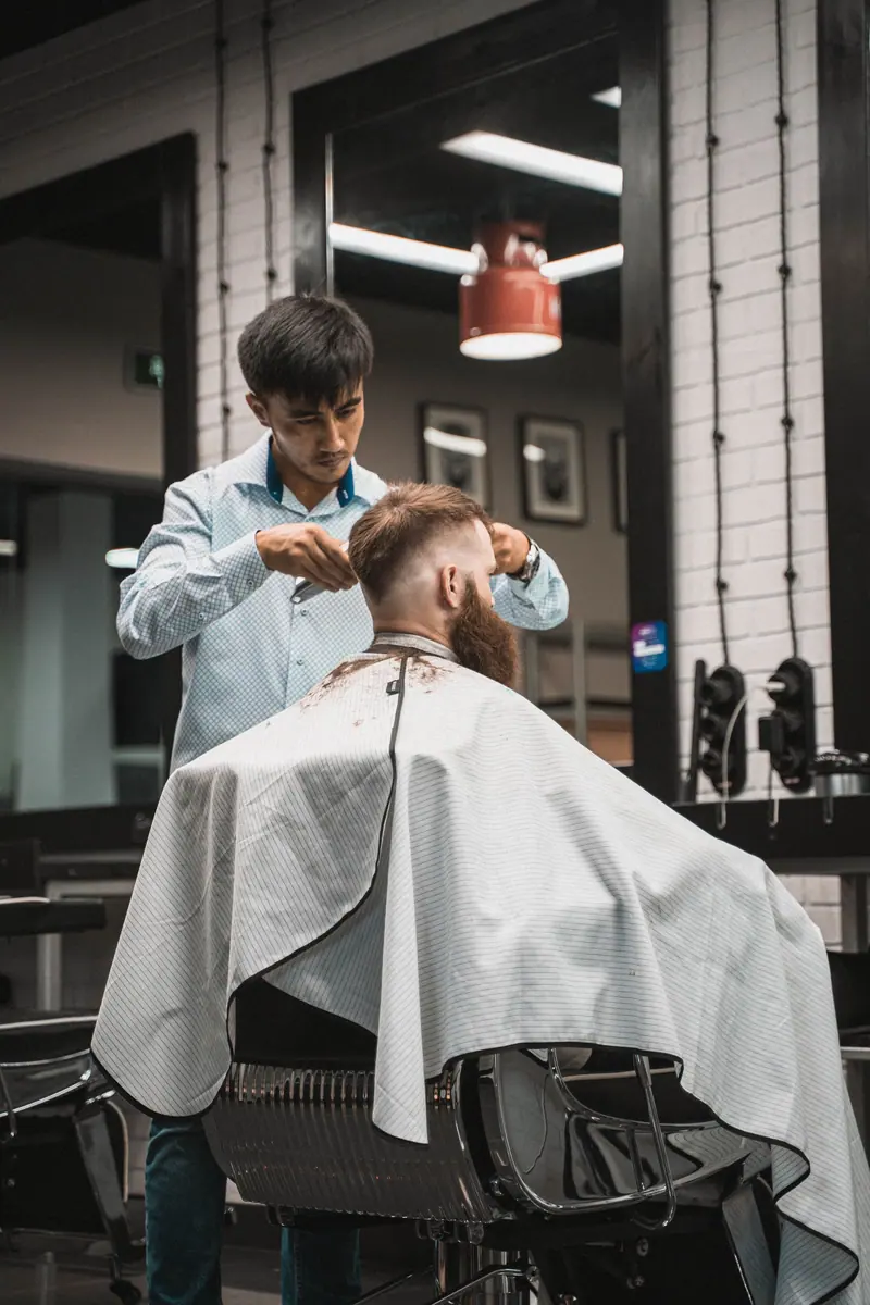 A barber carefully trims a client's hair in a modern, stylish salon setting.