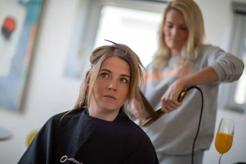 Woman in salon cape receiving professional hair styling indoors by hairdresser.