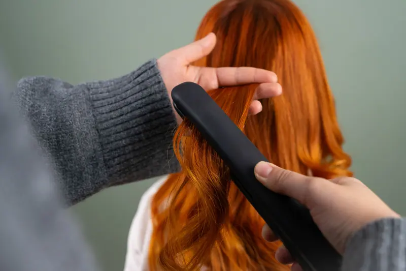 Flat-ironing glossy copper hair against a sage wall