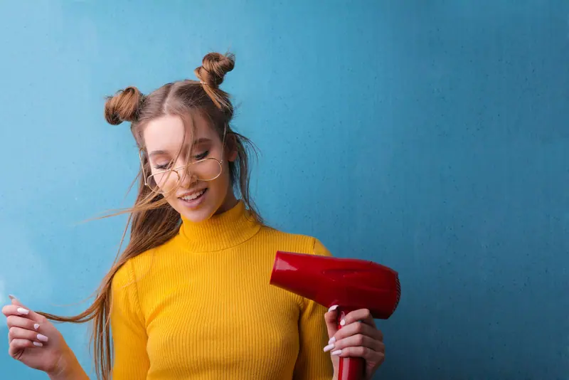 Smiling woman with a hair dryer and glasses against a bright blue wall