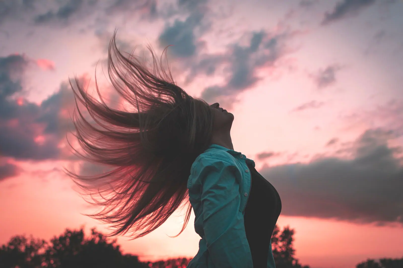 Woman flipping long hair against a pink and violet sunset sky