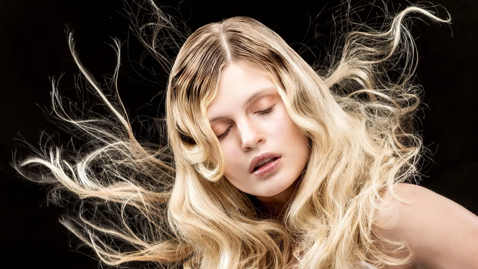 Woman with long, wind-swept platinum waves fanned out against a black background