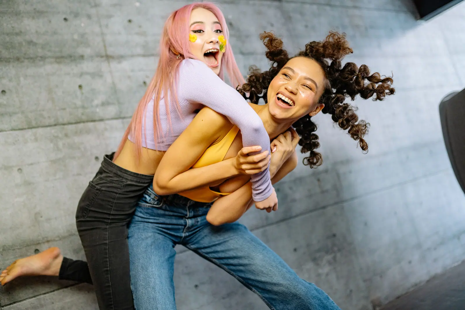 Two friends with pink and curly hair laughing together on a concrete studio floor