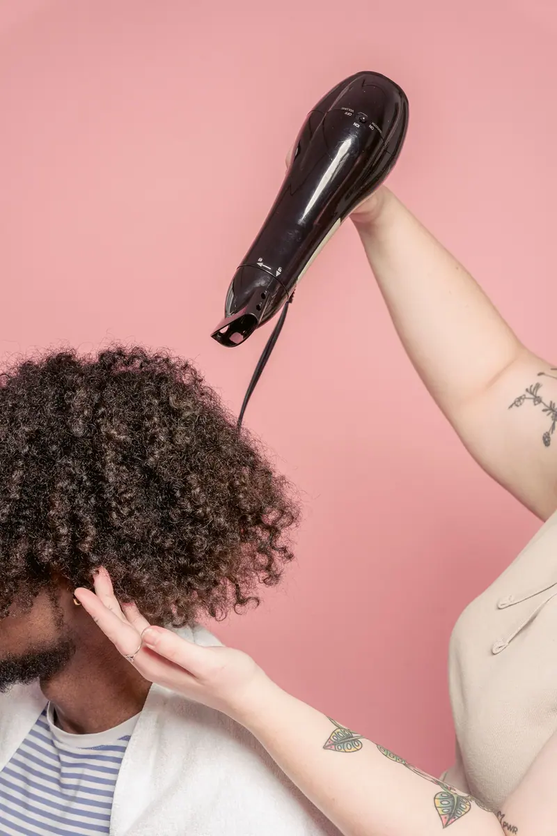 Blow-drying curls against a pink wall