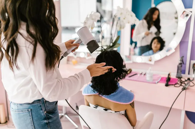 Stylist blow-drying a client's hair in a bright salon