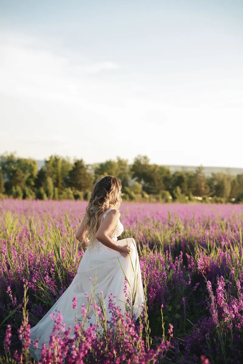 A woman in a wedding dress walks through a vibrant lavender field under a clear sky.