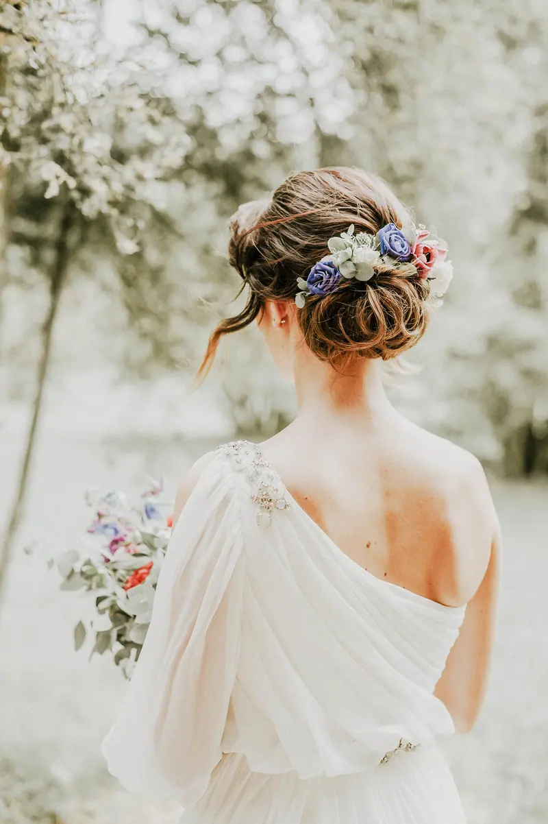 Bride with flowers in hair holding bouquet in serene outdoor setting.