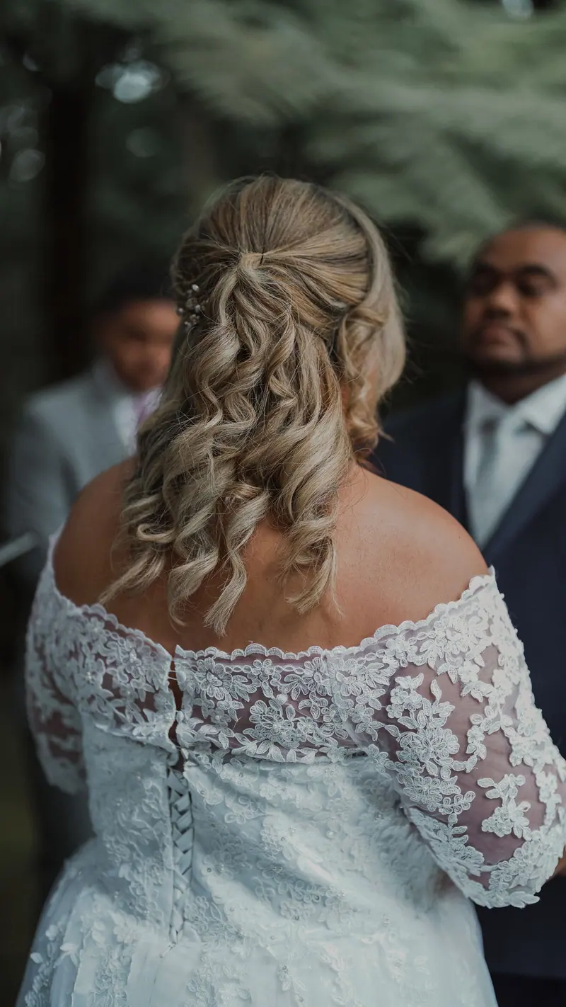 Back view of a bride in a lace wedding dress during an outdoor ceremony.