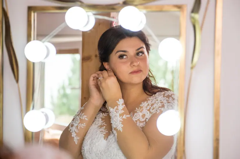 Bride adjusting earrings while looking at her reflection in a mirror before wedding.