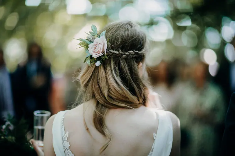 Elegant back view of a woman with braided hair and a floral accessory, outdoors.