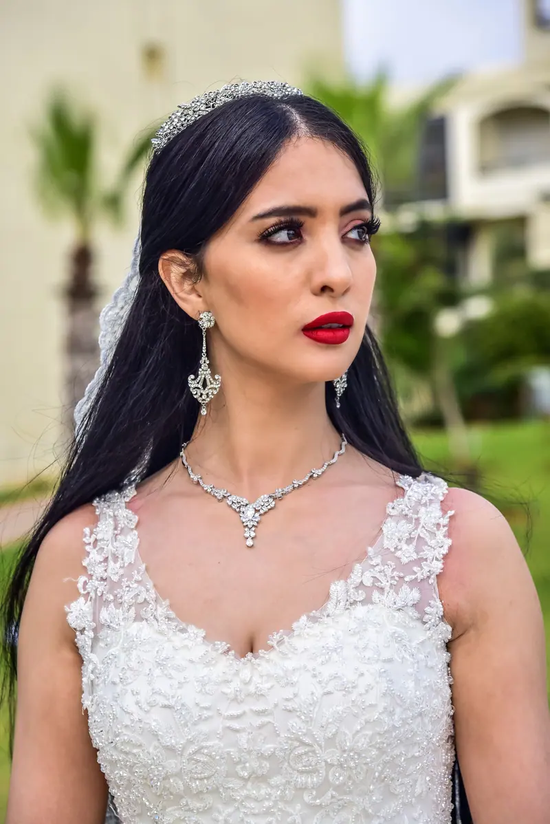 Beautiful bride with long black hair in a lace wedding dress outdoors.