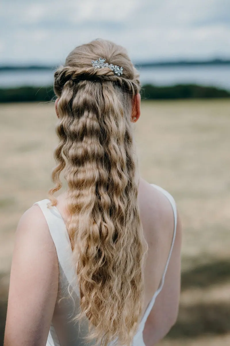A woman with long, wavy blonde hair seen from the back in an outdoor setting. White dress, summer vibe.