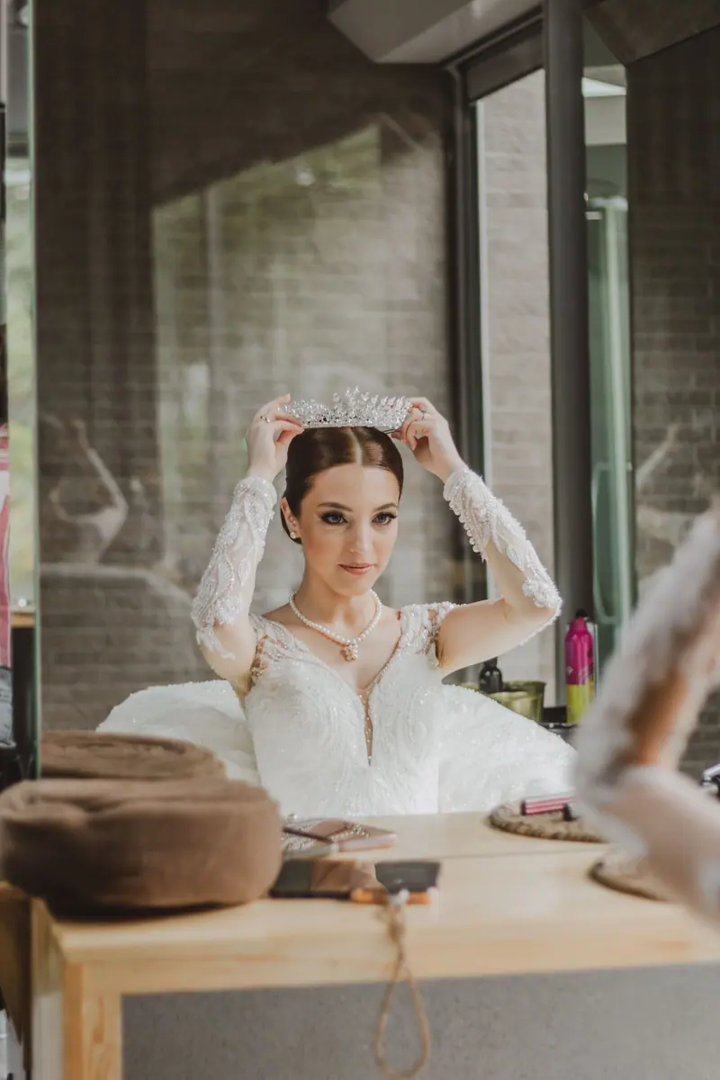 A bride in a lace wedding dress adjusts her tiara, preparing for her special day.