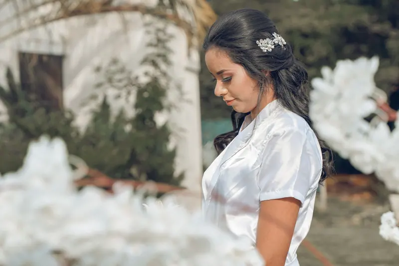 A bride in an elegant white dress poses outdoors with floral decorations.