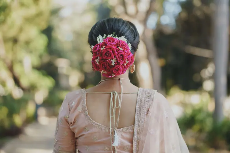 A woman in traditional attire with an elaborate floral hairstyle, captured outdoors.
