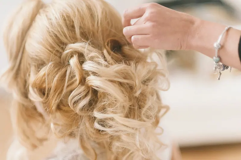 A professional hairstylist creates a blonde bridal updo for a wedding.